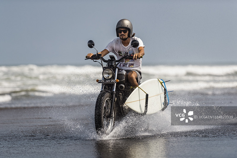 在巴厘岛海滩骑摩托车的不同种族男冲浪者图片素材