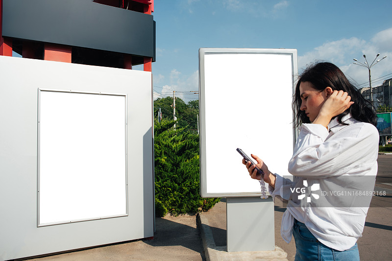 一位女士站在户外的广告banner旁。户外广告。城市。生活方式。文字和任何设计背景图片素材