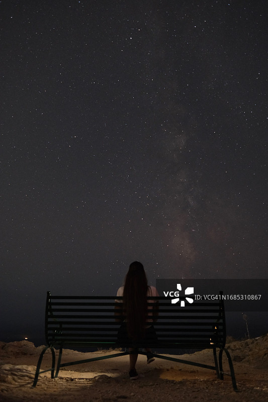 夜晚坐在长椅上，仰望星空银河的年轻女人图片素材