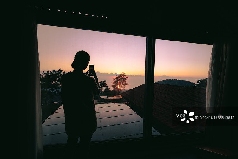 女人站在山间酒店房间里，用智能手机拍照图片素材