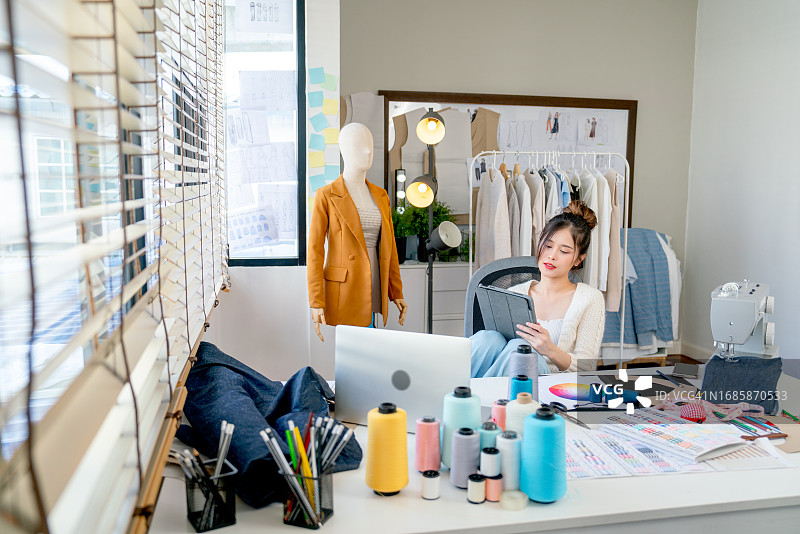 漂亮的亚洲设计师或裁缝女子坐在椅子上，手持平板电脑看着镜头图片素材