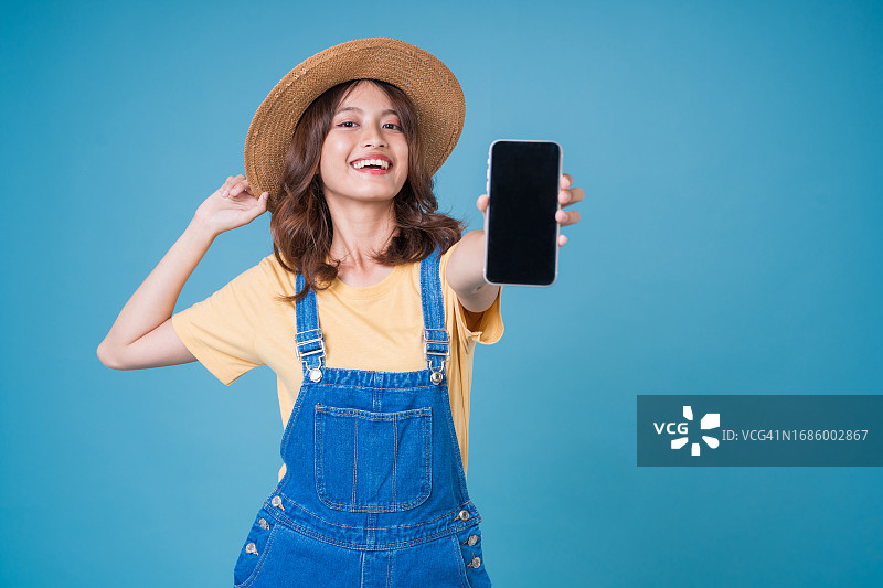戴夏帽和休闲装的年轻女人，手持带空白屏幕的手机图片素材