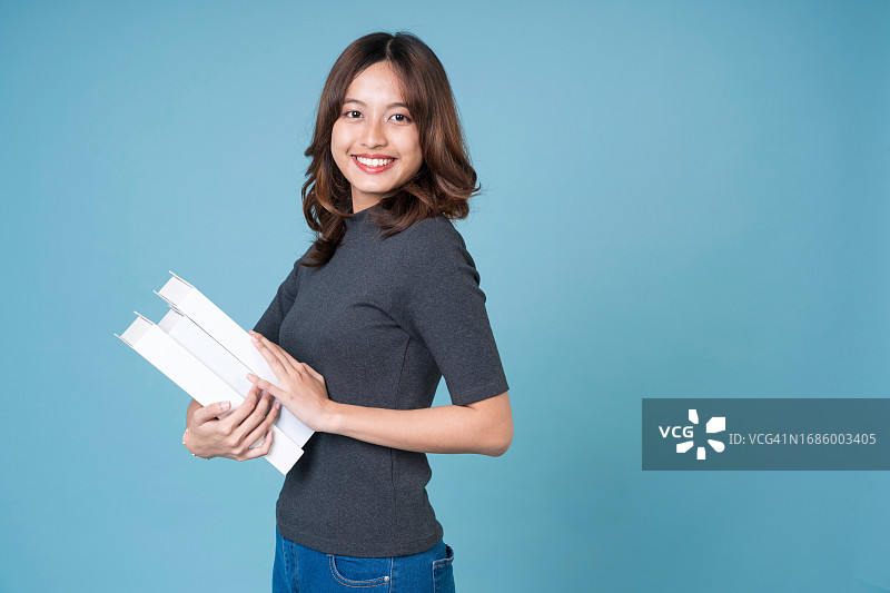 女学生拿着书站在浅蓝色背景前微笑。快乐的学校老师拿着书图片素材