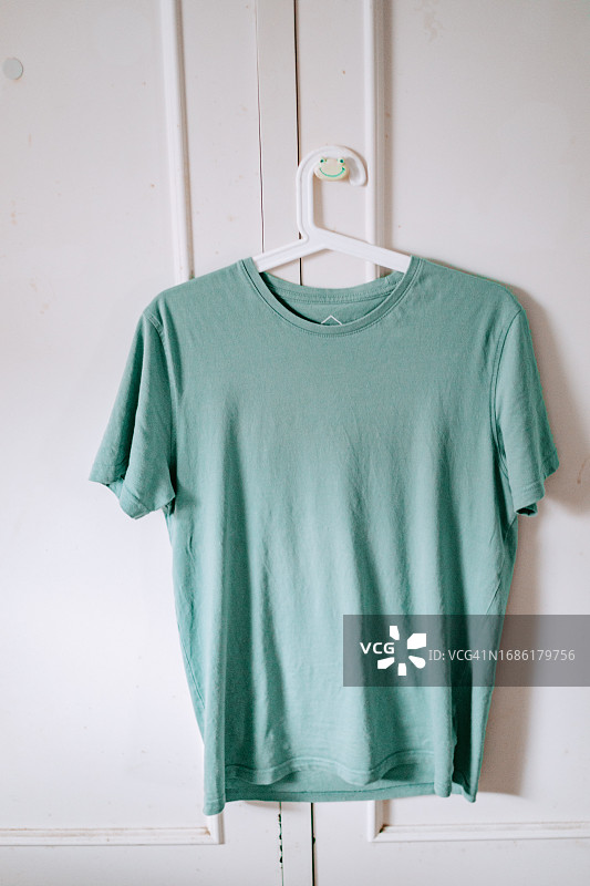挂在白色墙壁衣架上的绿色T恤图片素材
