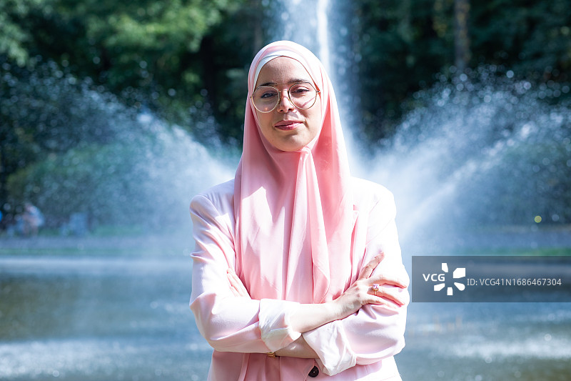 喷泉背景下，身着粉色服装和头巾的穆斯林Z世代女子图片素材