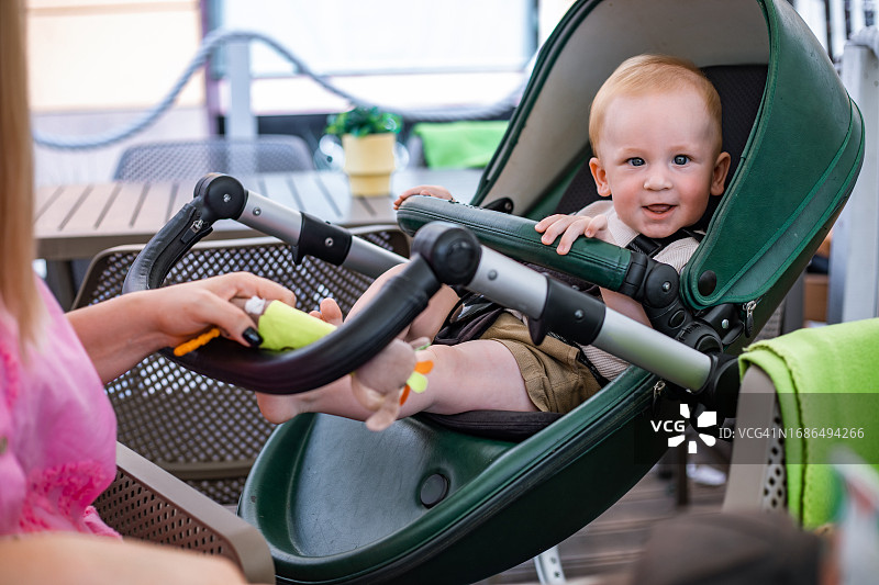 可爱的男婴坐在绿色婴儿车里，离穿着粉色衬衫的母亲不远图片素材