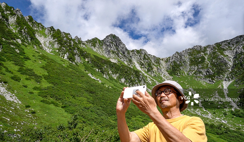 亚洲老人用智能手机在夏季高山拍照图片素材
