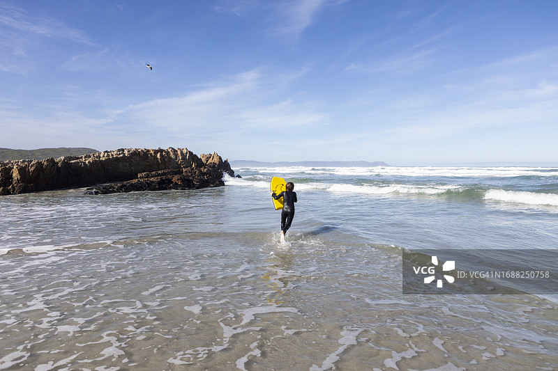 南非赫曼努斯：男孩在卡玛拜海滩带着趴板进入大西洋图片素材