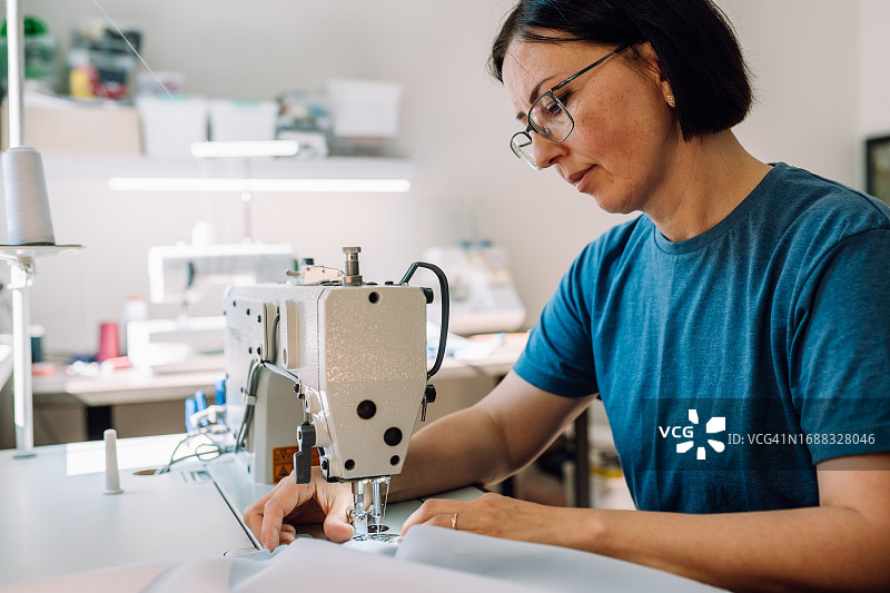 服装制造：中年妇女在明亮的工作室里使用缝纫机图片素材