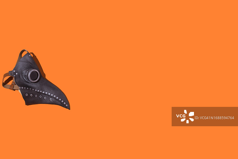 橙色万圣节背景上的皮革黑死病鸟嘴面具图片素材