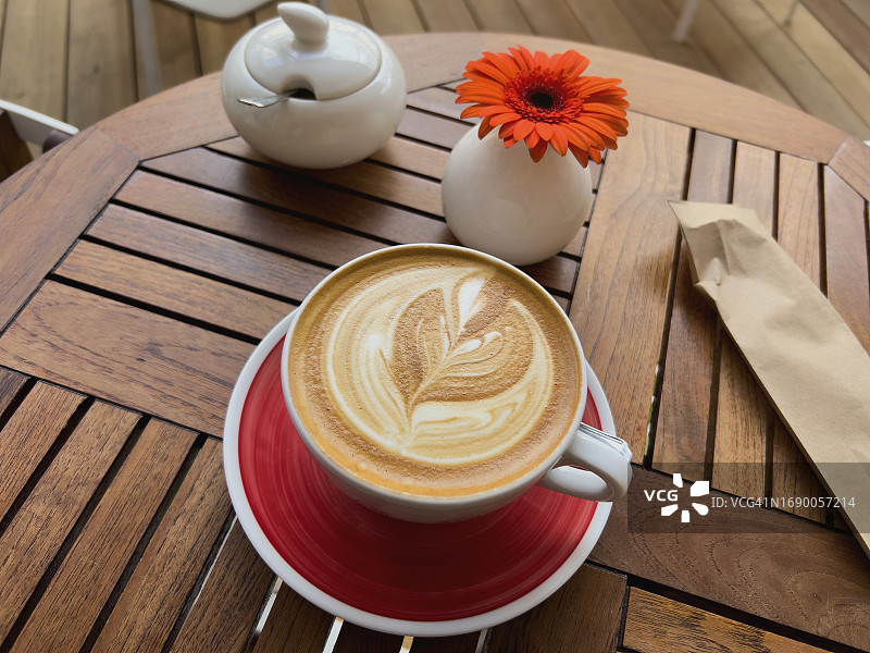 阳光明媚的夏日，当地小咖啡馆木桌上的拿铁艺术卡布奇诺咖啡图片素材