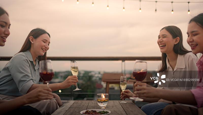 快乐的年轻亚洲女性团伙在屋顶酒吧派对上喝酒。女孩们在露台派对上玩得很开心图片素材