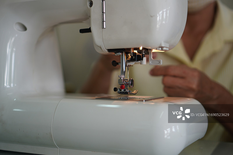 女人的手在缝纫机上操作配件设备，白色织物特写图片素材