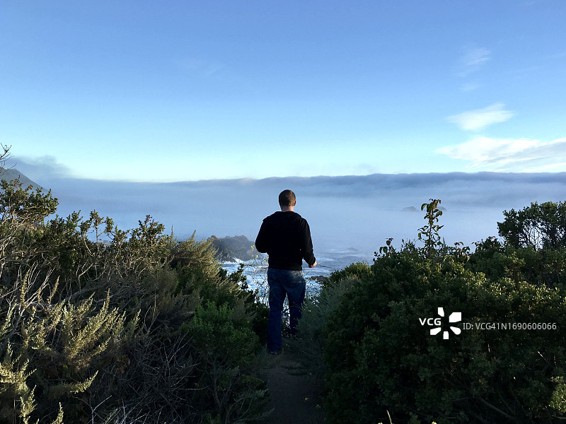 年轻男子背影，站在美国加州蒙特雷半岛沿海岩石上，1号公路图片素材