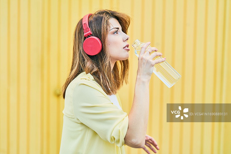 年轻女孩在黄色背景下饮用瓶装水特写图片素材