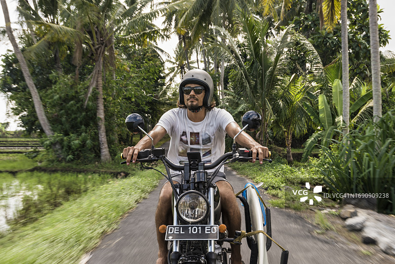 在巴厘岛小路上骑摩托车的不同种族男性冲浪者图片素材