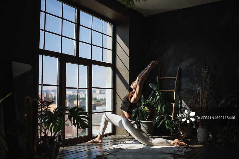 美丽的女人沐浴在从宽敞窗户流泻的自然光中，优雅地摆出战士一式姿势图片素材