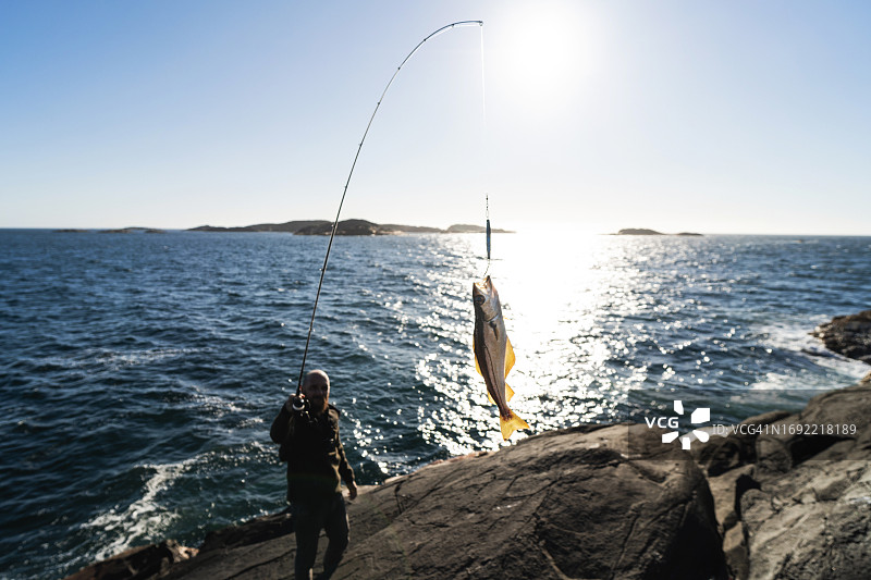 男人在海边的岩石上用钓竿钓鱼图片素材