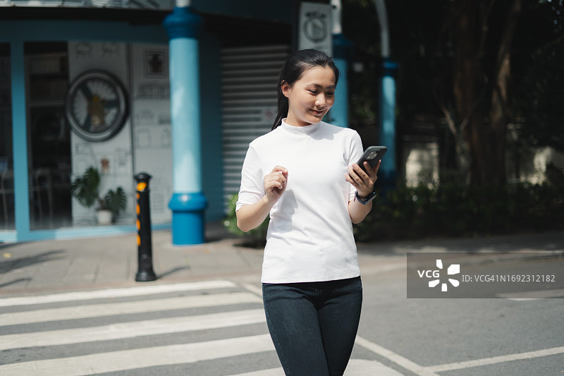 亚洲女性在城市里走路时高兴地笑着使用智能手机图片素材