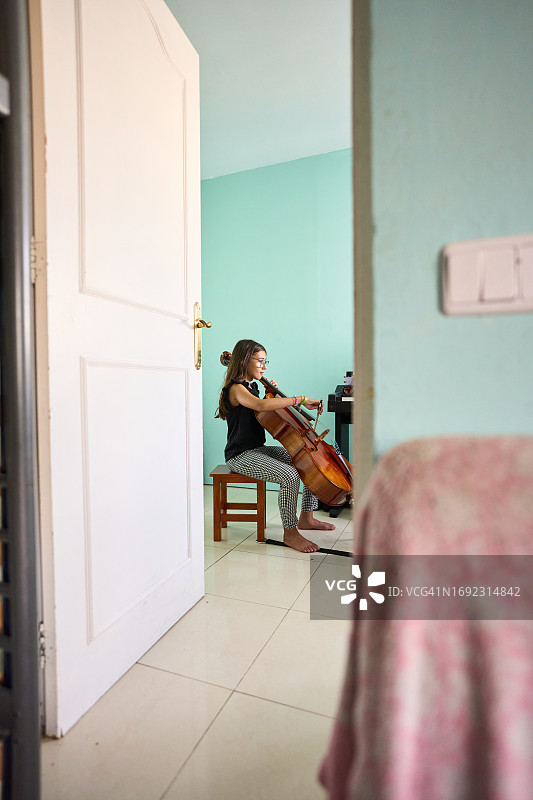 女孩在门打开的房间里演奏大提琴图片素材