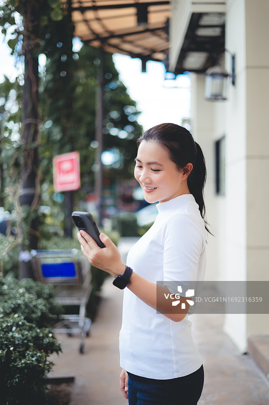 亚洲女性在城市里走路时高兴地笑着使用智能手机图片素材