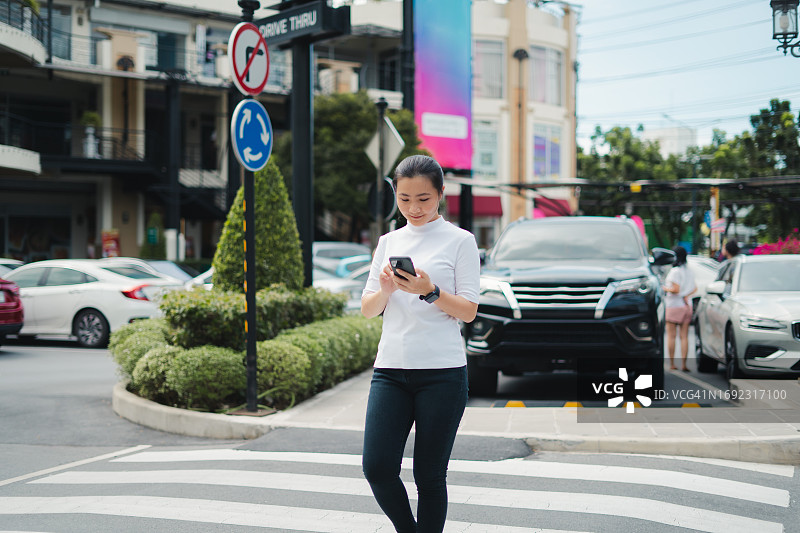 亚洲女性在城市里走路时高兴地笑着使用智能手机图片素材