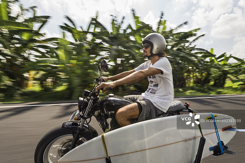 在巴厘岛小路上骑摩托车的不同种族男性冲浪者图片素材