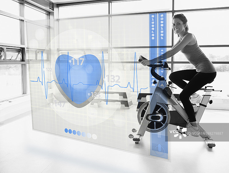 年轻有魅力的女孩使用带有未来界面的健身单车图片素材