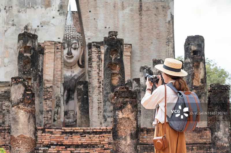 亚洲女游客在素可泰历史公园的西春寺内，拍摄有顶建筑内标志性巨型佛像图片素材