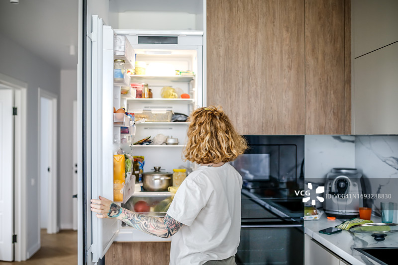 红发女人在家中打开的冰箱前图片素材
