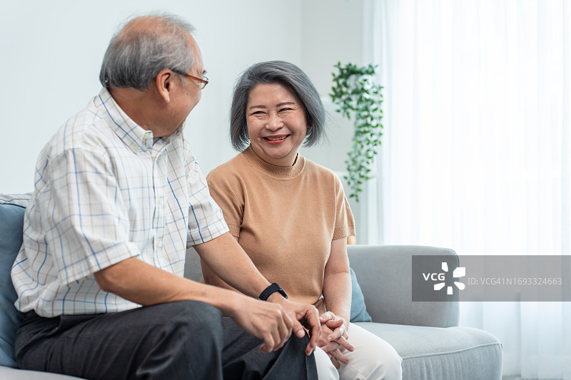 亚洲老年夫妇在客厅里交谈和坐在沙发上，慈爱的老人在家中享受退休生活图片素材