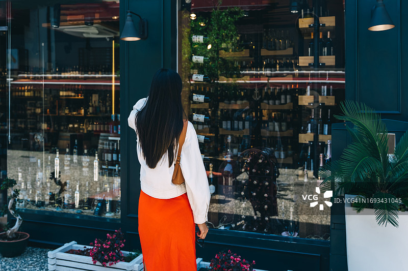 穿着鲜艳T恤的年轻亚洲女性在商店橱窗里挑选珠宝。图片素材