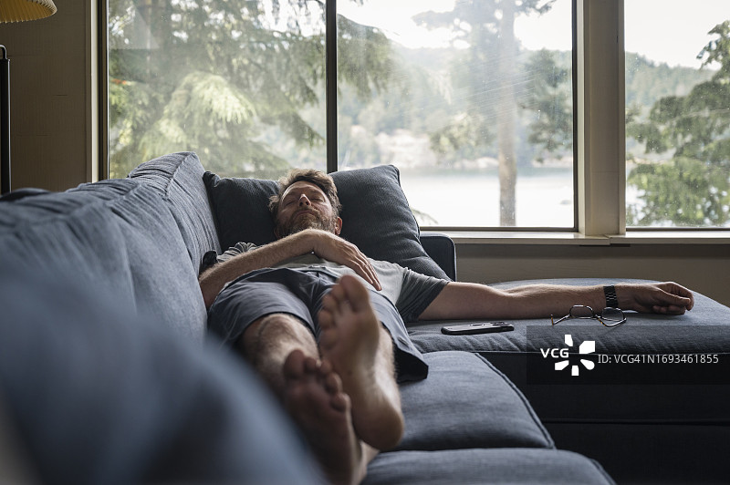 男人睡在蓝色沙发上，旁边放着眼镜和手机图片素材