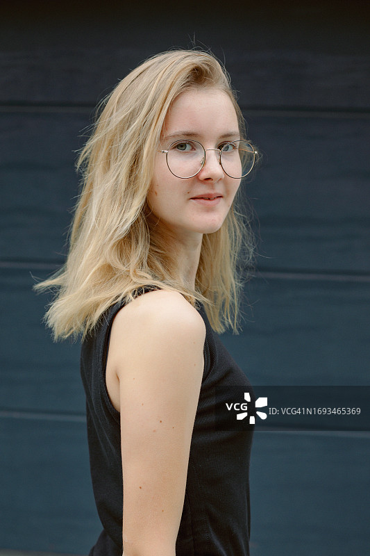 站在深灰色墙前的金发眼镜少女肖像图片素材