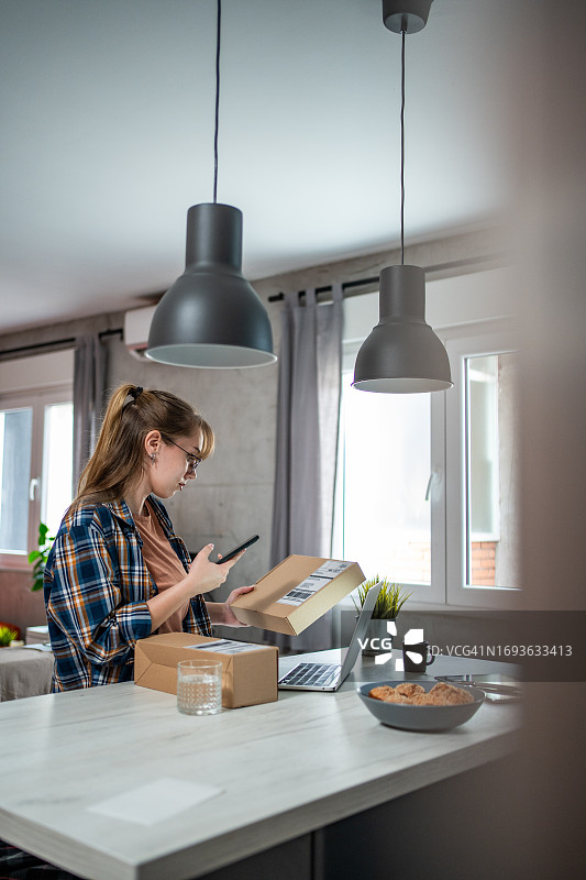 一位年轻女子正在检查一个刚到家的包裹，这是她在网上订购的图片素材
