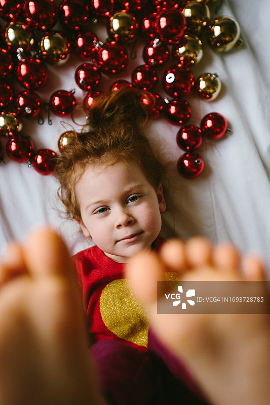 红发女孩躺在白色床单上，周围是圣诞球图片素材