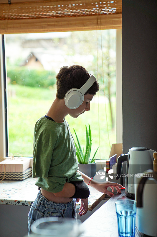 手臂骨折的少年在厨房打开电热水壶图片素材