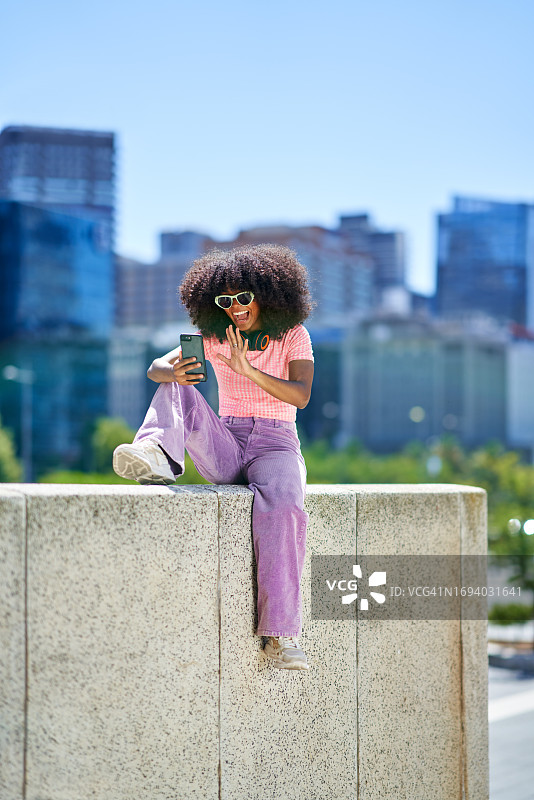 快乐的年轻女人在阳光明媚的城市用智能手机进行视频聊天图片素材