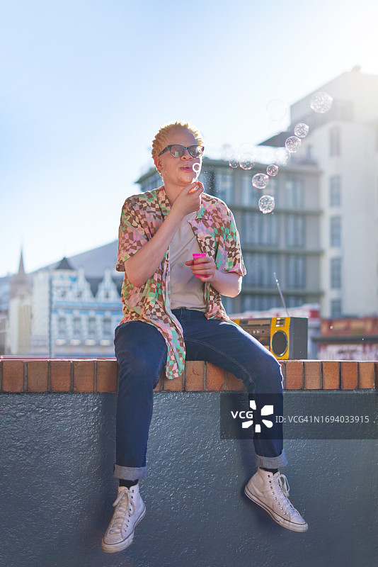 阳光明媚的城市阳台上，年轻男人正在吹泡泡图片素材