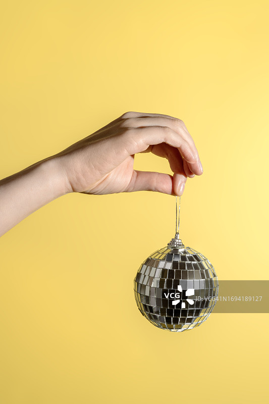 拥有自然美甲的美丽女性手拿着银色迪斯科球。人手中的圣诞树玩具。节日快乐庆祝活动。具有复制空间的抽象简约背景图片素材