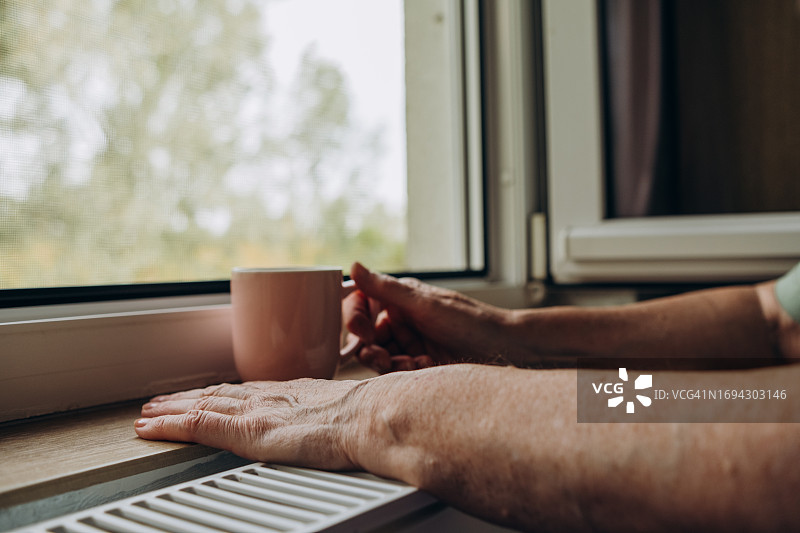 家中暖气问题，老年妇女试图在加热器附近取暖图片素材