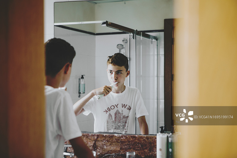 青少年男孩在浴室用电动牙刷刷牙图片素材