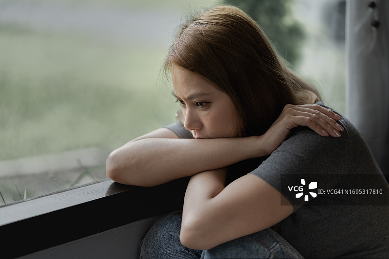 坐在大窗户旁，脸上带着悲伤表情的沮丧女人图片素材