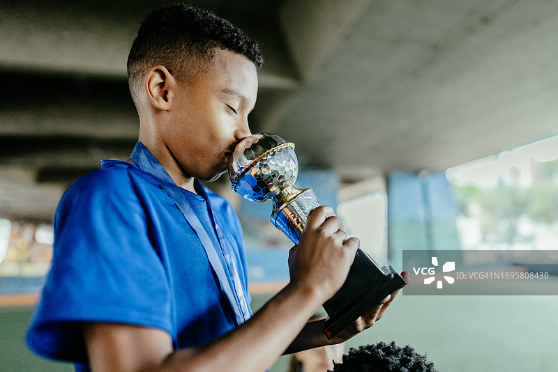 足球运动员在足球场上亲吻奖杯图片素材