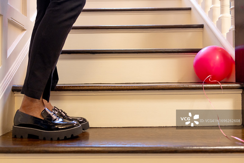 黑人女性站在台阶上，穿着黑色裤子和乐福鞋，对面是粉色气球图片素材