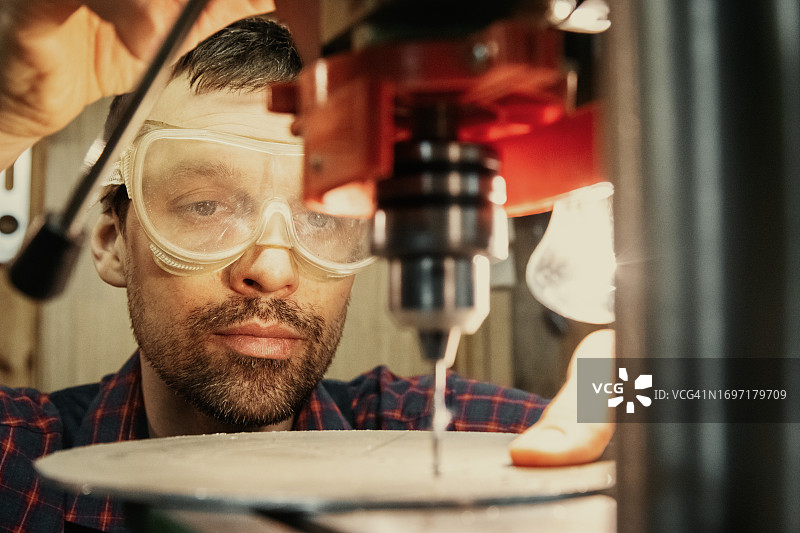 戴着安全眼镜的工人在车间使用钻机钻孔图片素材