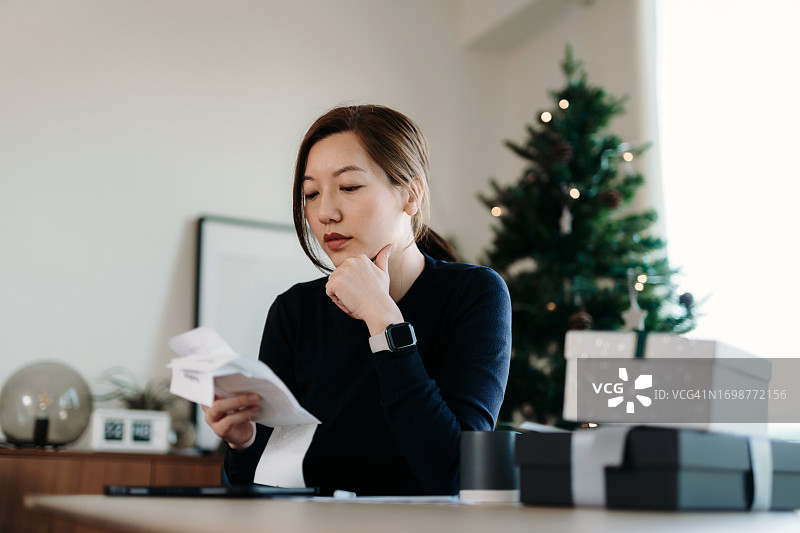 圣诞节购物后，年轻亚裔女性查看各种费用收据和账单时感到压力，对个人银行和财务感到焦虑，在家计划预算、计算支出和管理财务账单图片素材