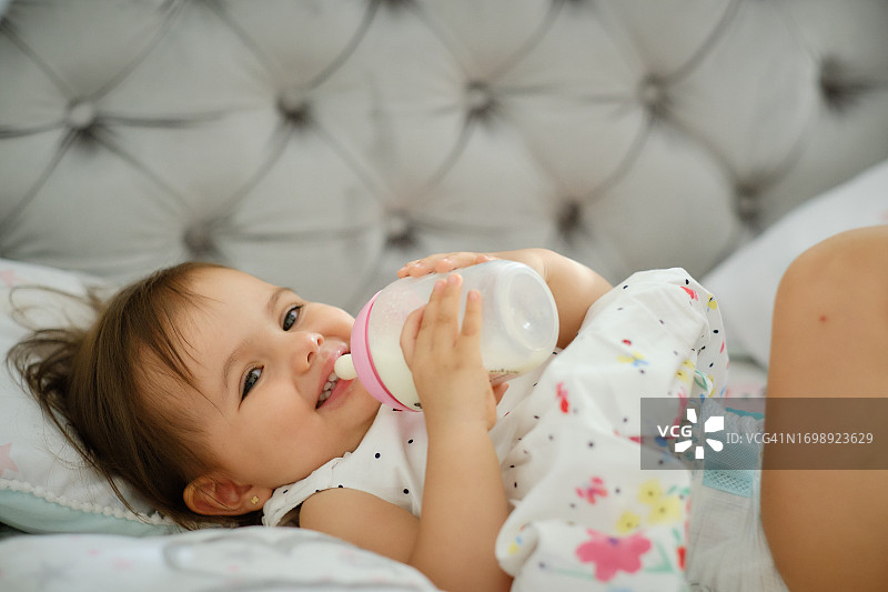 小女孩躺在床上拿着奶瓶，看着妈妈微笑图片素材