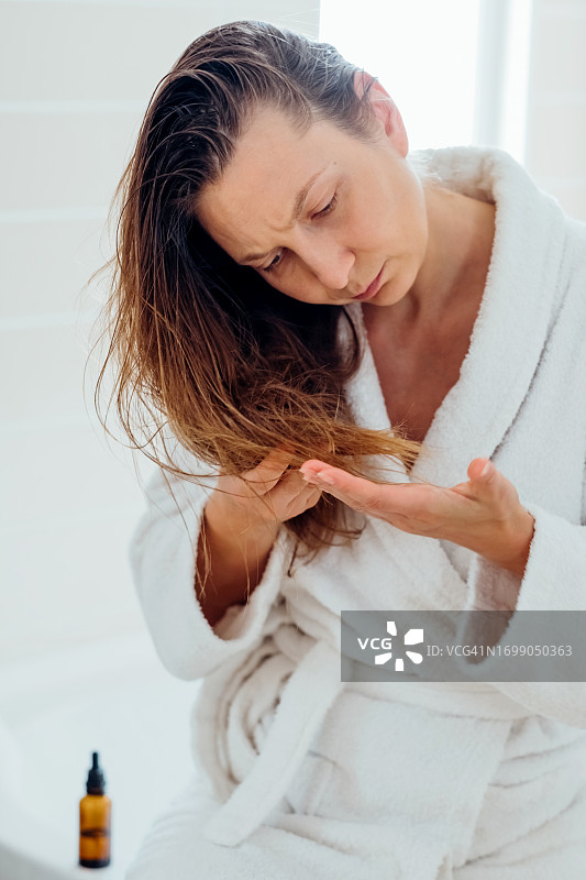 年轻女子评估干燥受损头发的开叉，强调居家护理理念图片素材