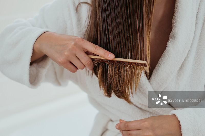 女士用木梳仔细梳理头发特写，护理头发分叉。图片素材